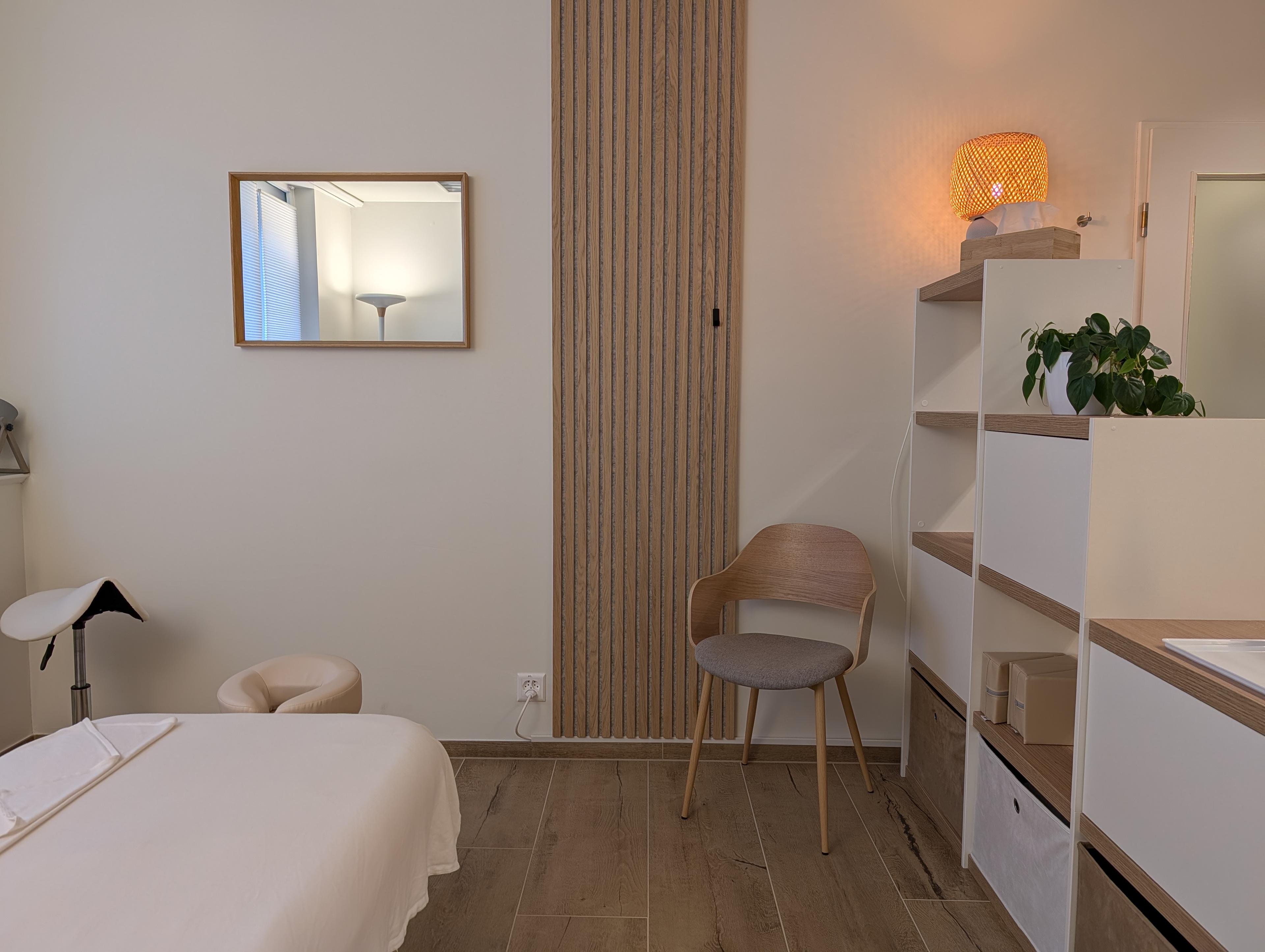 Massageraum in der Praxis origin Massage Oerlikon Bahnhof mit Liege, Wandspiegel, Holzlamellenwand und offenem Regal mit Pflanzen und dekorativer Lampe.