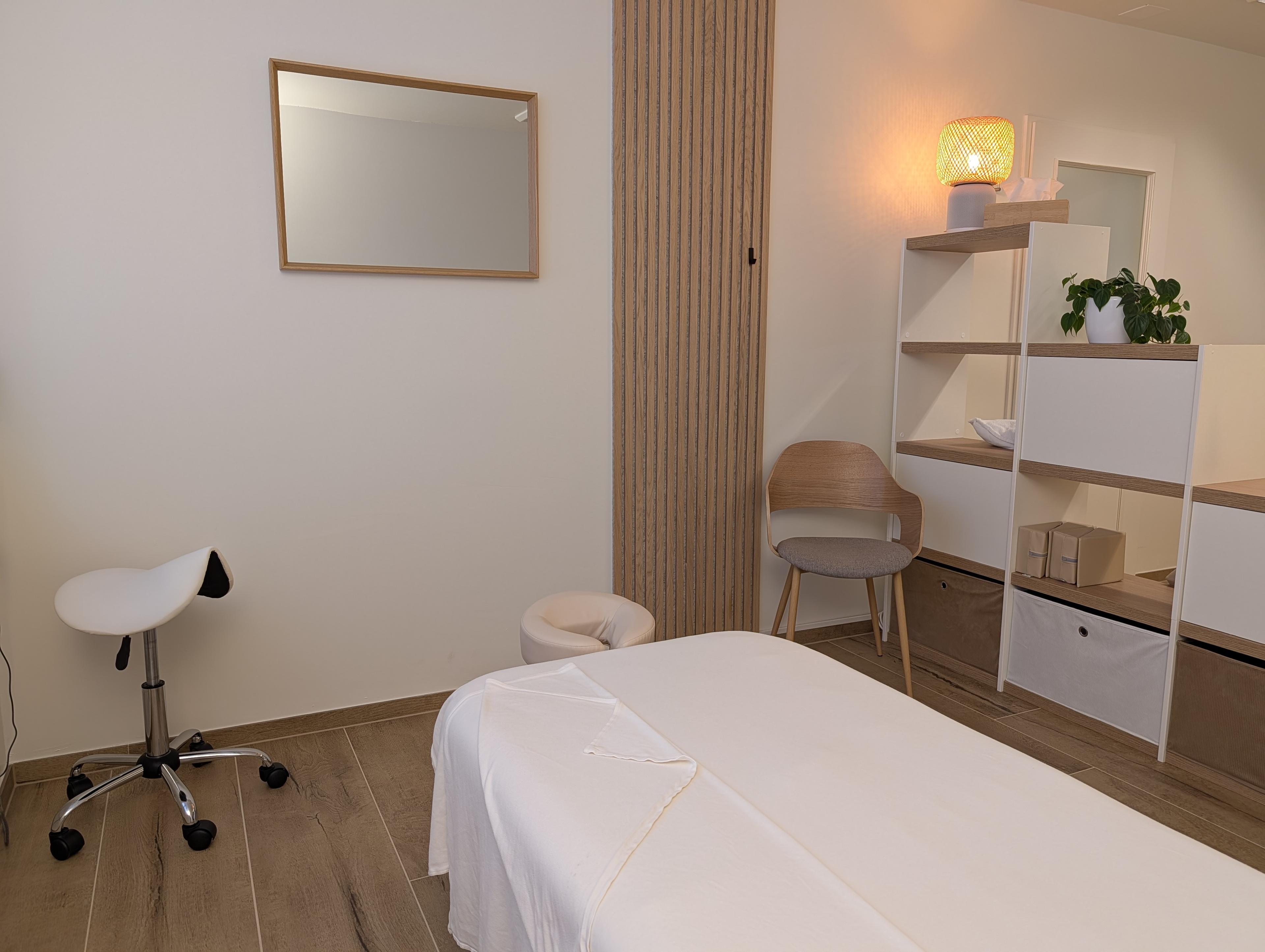 Behandlungsraum der Praxis Origin Massage Oerlikon Bahnhof mit Massageliege, Holzregal, warmer Beleuchtung und minimalistischem Design in Naturtönen.
